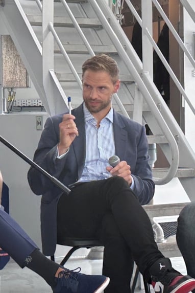 fire menn som sitter på rekke om bord på en båt. To av dem holder mikrofoner. Foto
